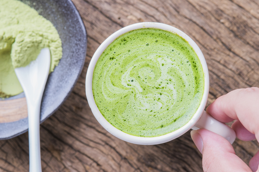 Hot green tea latte with matcha powder on wooden background.