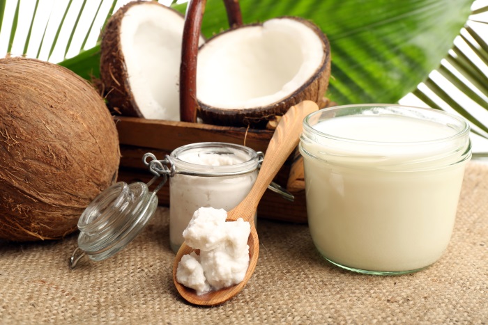 Coconut with jars of coconut oil and milk on sackcloth on natural background